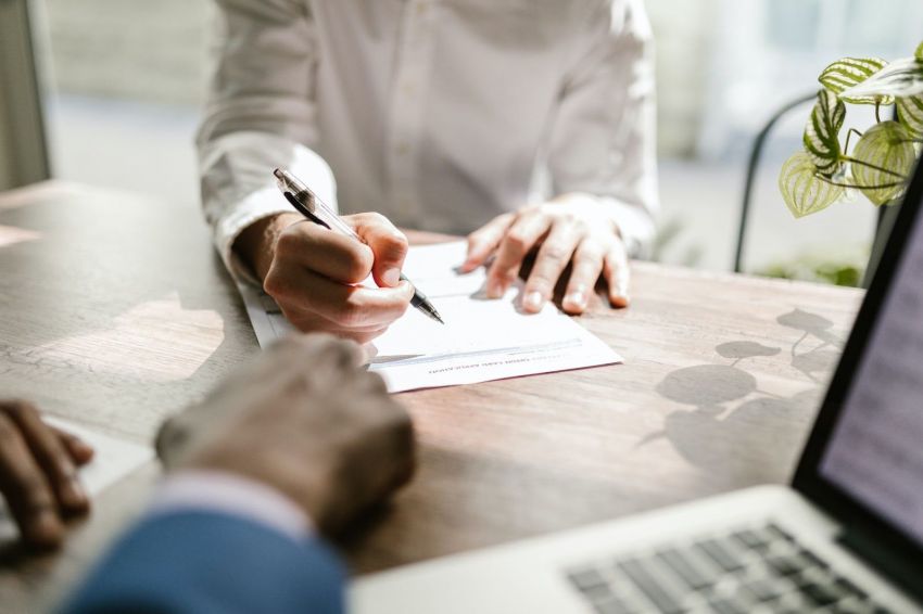 Women and a man sitting at a desk with a laptop signing important documents